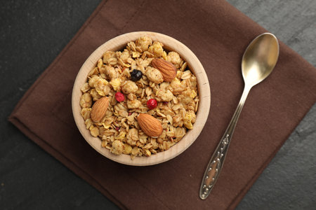 Tasty granola with dried fruits and nuts in bowl on black table, flat lay