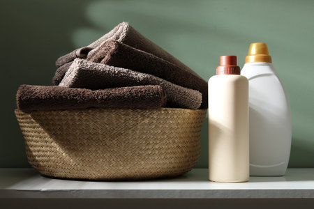 Laundry basket with towels and bottles of detergent on dresser near green wall indoors