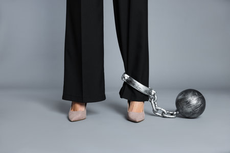 Businesswoman with metal ball and chain on her leg against gray background, closeup