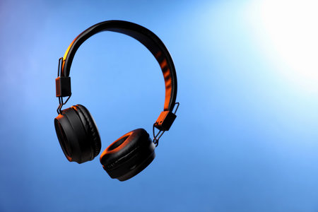 Pair of stylish headphones in air on light blue gradient background, space for textの写真素材