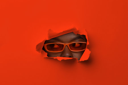 Young woman with sunglasses, view through torn hole in red paper