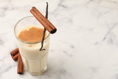 Protein shake in glass, cinnamon and vanilla pod on white marble table, closeup. Space for textの写真素材