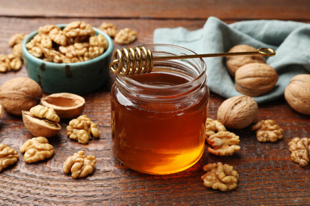 Honey in jar, dipper and walnuts on wooden table, closeupの写真素材