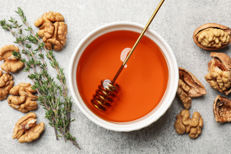 Honey in bowl, walnuts and thyme on light gray table, flat layの写真素材