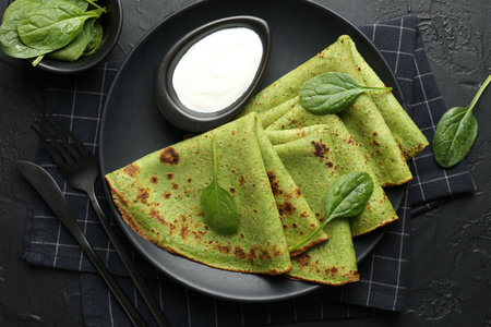 Tasty spinach crepes with sour cream and leaves on black table, flat layの写真素材