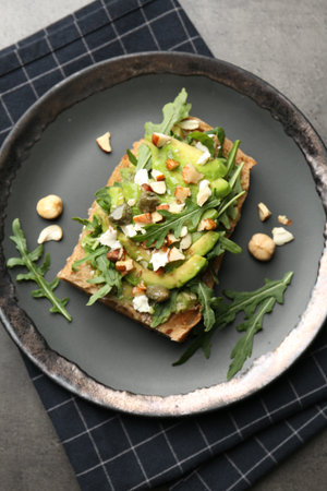 Tasty bruschetta with avocado, arugula, nuts and feta cheese on gray table, top view