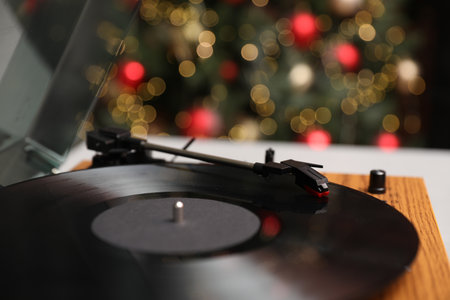 Turntable with vinyl record on table near Christmas tree, closeup