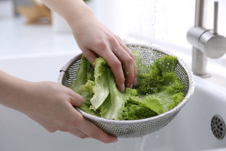 Woman washing lettuce in sieve at sink, closeup