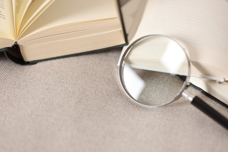 Magnifying glass and books on sofa, closeup