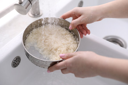 Woman washing rice in sieve at sink, closeup