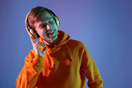 Man with headphones listening to music on blue background in neon lights. Space for text