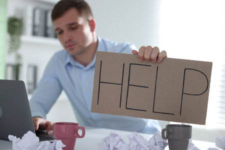 Man with laptop and sign Help at table in office, selective focusの写真素材
