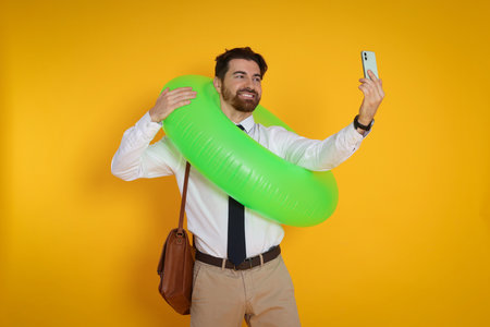 Man with inflatable ring and briefcase having video chat via smartphone on orange backgroundの写真素材