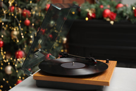 Turntable with vinyl record on table near Christmas tree, closeup