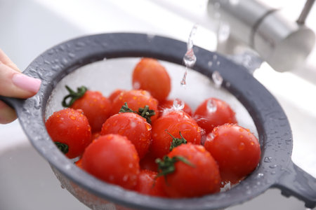 Woman washing cherry tomatoes in sieve at sink, closeup