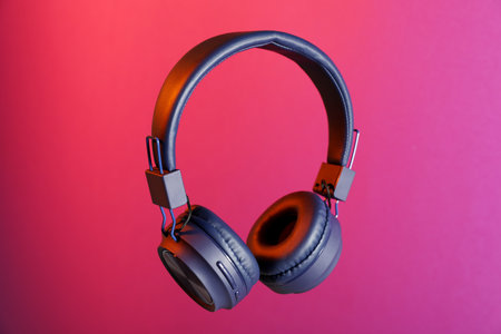 Pair of stylish headphones in air on bright pink background