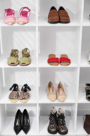 Different pairs of shoes on shelves near white wall indoorsの写真素材