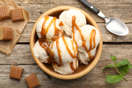 Tasty ice cream with caramel sauce and mint in bowl on wooden table, flat layの写真素材