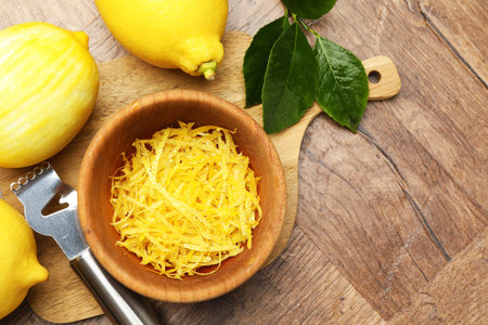 Lemon zest, fresh fruits and zester tool on wooden table, flat lay. Space for text