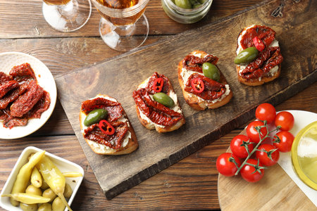 Delicious bruschettas with cream cheese, sun-dried tomatoes, chili pepper and green olives on wooden table, flat layの写真素材