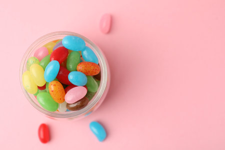 Delicious colorful candies in jar on pink background, top view. Space for text