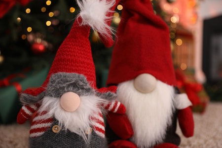 Cute Christmas gnomes against blurred lights indoors, closeup