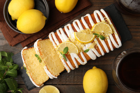 Delicious lemon cake with glaze, fresh fruit slices and mint on wooden table, flat layの写真素材
