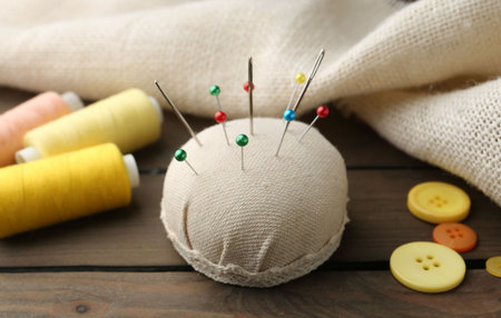 Pincushion with pins, needles, spools of threads, buttons and cloth on wooden table, closeupの写真素材