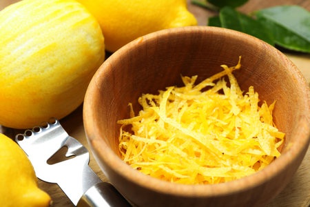 Lemon zest, fresh fruits and zester tool on wooden table, closeup