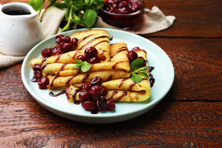 Delicious crepes served with cherry jam and chocolate on wooden table, closeupの写真素材