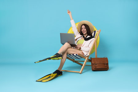 Woman with laptop and flippers in deck chair on light blue background