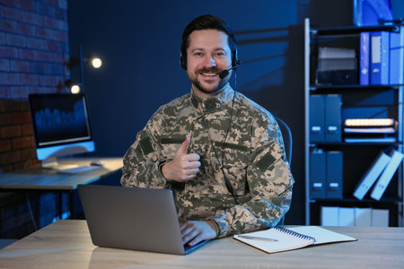 Military man showing thumbs up at wooden desk in office at nightの写真素材
