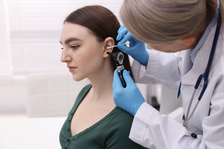 Hearing test. Doctor examining patient's ear with otoscope and cotton swab in clinicの写真素材