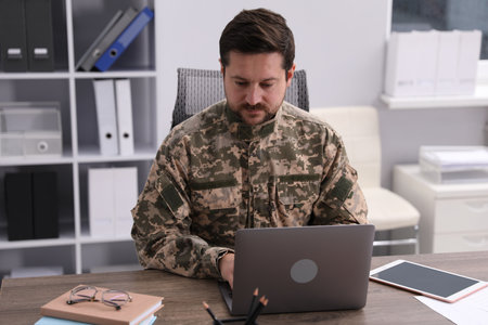 Military education. Student in soldier uniform learning at wooden desk indoors