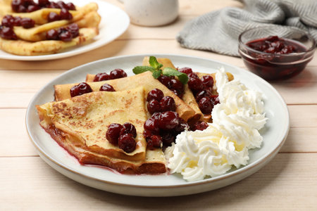 Tasty crepes with cherries, whipped cream and mint served on white wooden table, closeupの写真素材