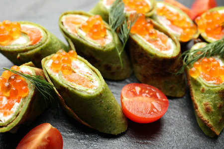 Tasty spinach crepes with salmon, cream cheese, tomatoes and dill on table, closeupの写真素材