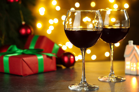 Glasses of red wine and Christmas decor on wooden table against background with blurred lightsの写真素材