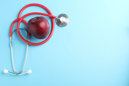 Ripe apple and stethoscope on light blue background, flat lay. Space for textの写真素材