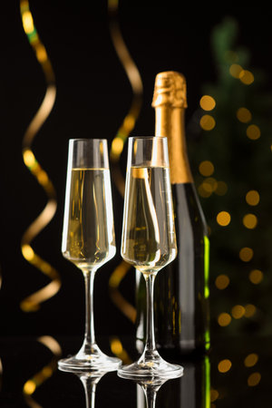 Merry Christmas and Happy New Year. Flute glasses with sparkling wine, serpentine streamers and bottle on black background against blurred lightsの写真素材