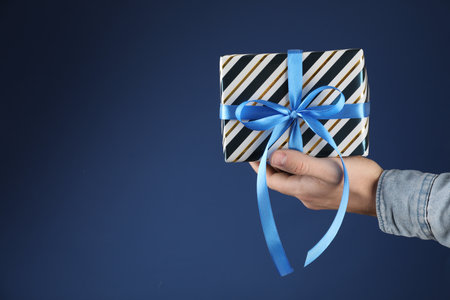 Man with beautiful gift box on blue background, closeup. Space for textの写真素材