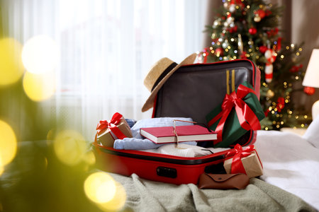 Suitcase with clothes, other stuff and gifts on bed in festive decorated room. Christmas vacationの写真素材