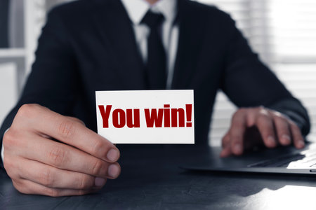 Businessman holding card with the phrase You Win! at table in office, closeupの写真素材