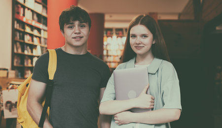 Students in campus library. Teenage boy with backpack and girl holding laptopの写真素材