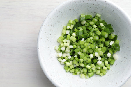 Cut fresh green onions in bowl on light wooden table, top view. Space for textの写真素材
