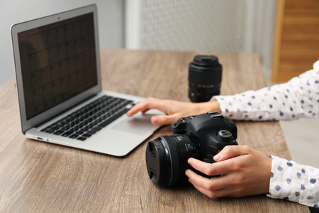 Professional photographer with laptop, camera and lens at wooden table, closeupの写真素材