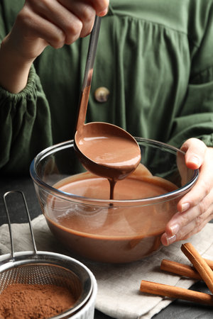 Woman taking liquid chocolate dough ladle at table, closeupの写真素材
