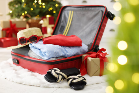 Suitcase with clothes, sunglasses, shoes and gifts on floor in festive decorated room, closeup. Christmas vacationの写真素材