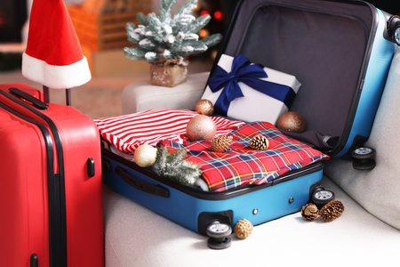 Suitcases with clothes, gift and festive decor on sofa indoors, closeup. Christmas vacationの写真素材