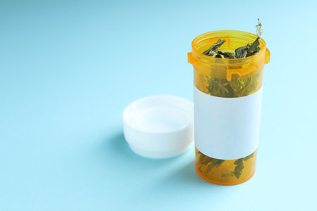 Dried hemp leaves in plastic bottle on light blue background, closeup. Space for textの写真素材