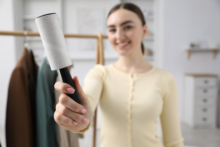 Woman with lint roller near rack with clothes at home, selective focusの写真素材